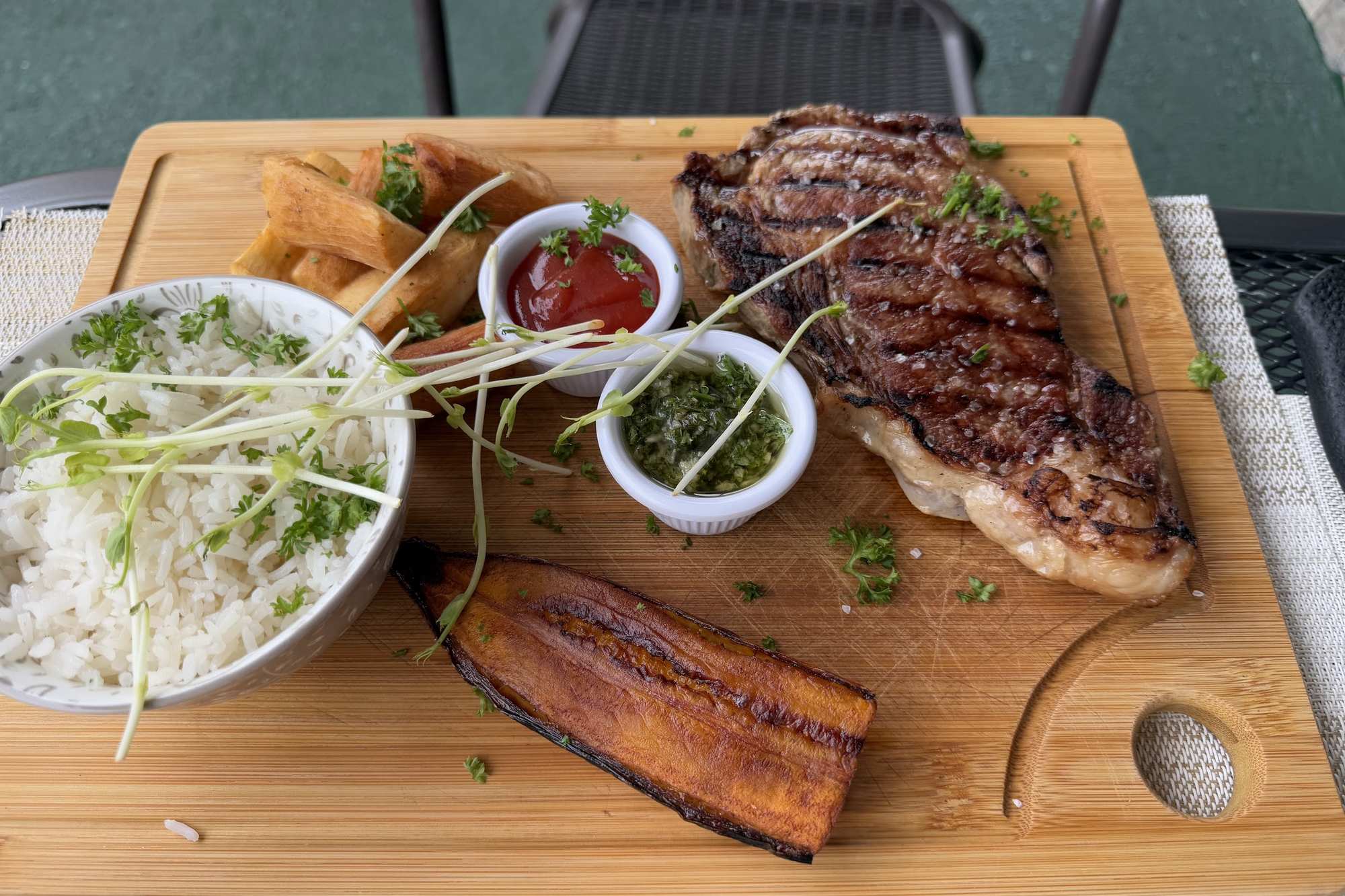 Lomo a la parrilla con arroz, plátano y chimichurri servido en tabla de madera en Harmony Food